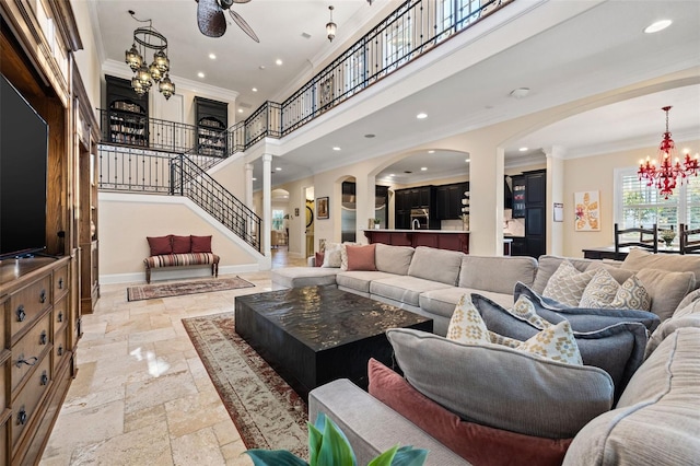 living room featuring a towering ceiling, baseboards, an inviting chandelier, stone tile flooring, and crown molding