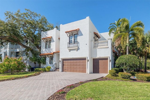 view of front of property with decorative driveway, an attached garage, a balcony, and stucco siding