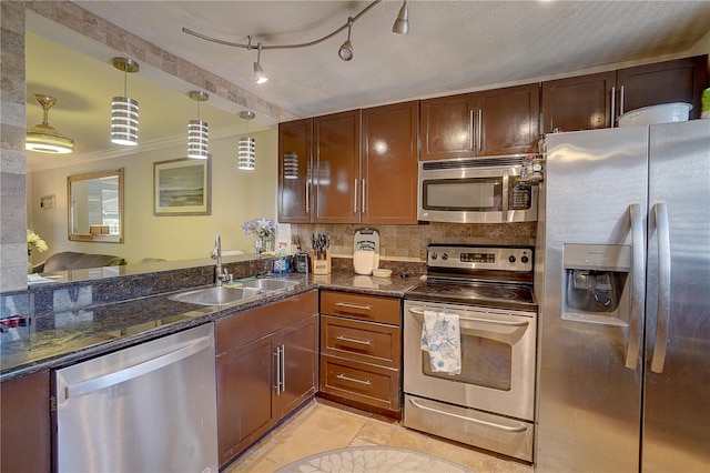 kitchen with pendant lighting, backsplash, appliances with stainless steel finishes, a sink, and dark stone countertops