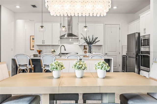 kitchen with visible vents, wall chimney exhaust hood, appliances with stainless steel finishes, white cabinetry, and backsplash