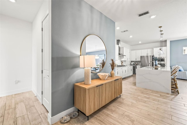 corridor with recessed lighting, visible vents, a sink, and light wood-style flooring