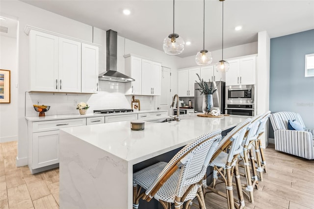 kitchen featuring wall chimney exhaust hood, appliances with stainless steel finishes, backsplash, and white cabinets