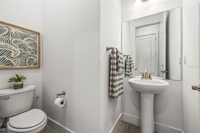 half bathroom featuring toilet, a sink, baseboards, and wood finished floors