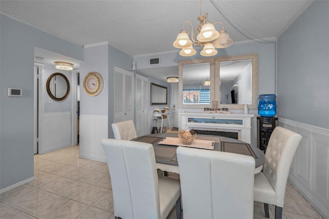 dining space with visible vents, a chandelier, a textured ceiling, and wainscoting