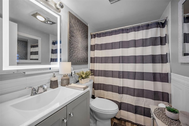 bathroom featuring toilet, curtained shower, wainscoting, and vanity