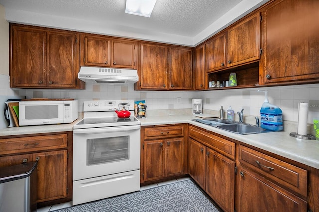 kitchen featuring under cabinet range hood, white appliances, a sink, light countertops, and decorative backsplash