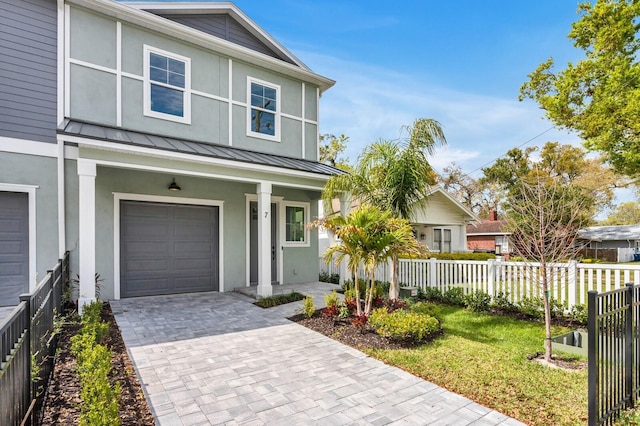 view of front of house featuring a garage, metal roof, a standing seam roof, fence, and decorative driveway