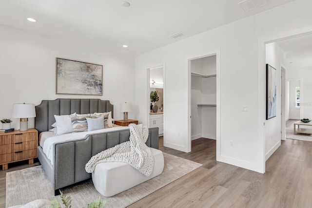 bedroom featuring recessed lighting, wood finished floors, visible vents, baseboards, and a walk in closet