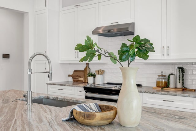 interior space with under cabinet range hood, a sink, stainless steel range with electric cooktop, white cabinets, and light stone countertops