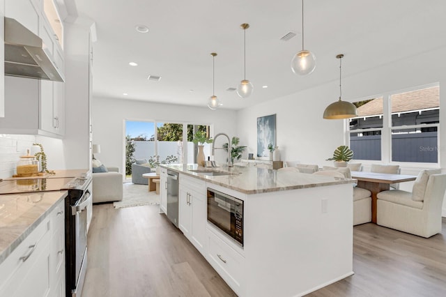 kitchen featuring black microwave, range with electric cooktop, a sink, open floor plan, and ventilation hood