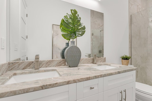 full bath featuring toilet, a sink, a marble finish shower, and double vanity