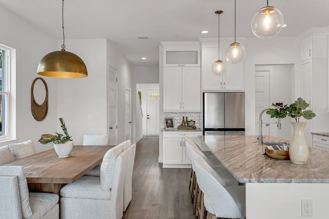 kitchen featuring dark wood-style floors, tasteful backsplash, freestanding refrigerator, white cabinetry, and light stone countertops