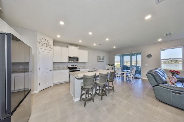 kitchen featuring a sink, visible vents, open floor plan, appliances with stainless steel finishes, and a center island with sink