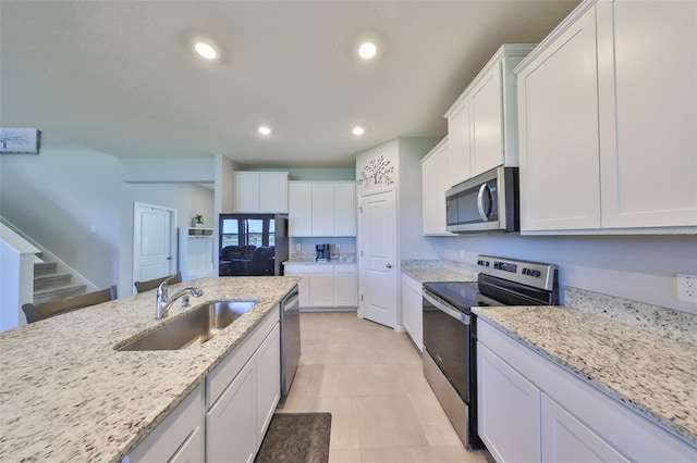 kitchen with recessed lighting, appliances with stainless steel finishes, white cabinets, a sink, and light stone countertops