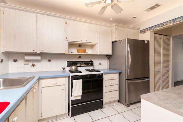 kitchen featuring range with gas cooktop, light tile patterned floors, visible vents, decorative backsplash, and freestanding refrigerator