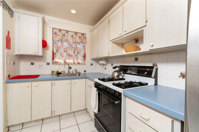 kitchen featuring range with gas stovetop, tasteful backsplash, light countertops, light tile patterned flooring, and a sink