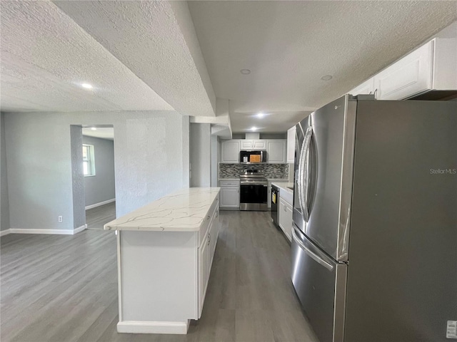 kitchen with appliances with stainless steel finishes, white cabinets, decorative backsplash, and wood finished floors