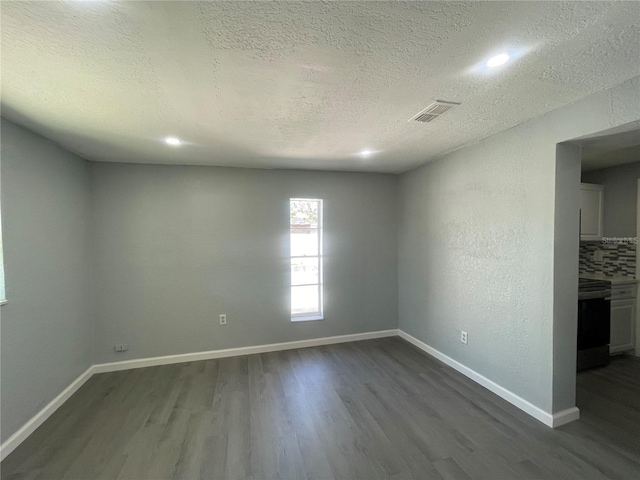 spare room with a textured ceiling, dark wood-style flooring, visible vents, and baseboards