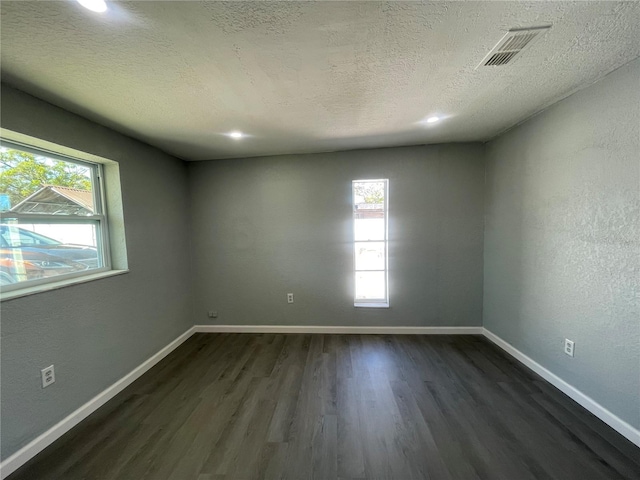 empty room with dark wood-style floors, a textured ceiling, visible vents, and baseboards