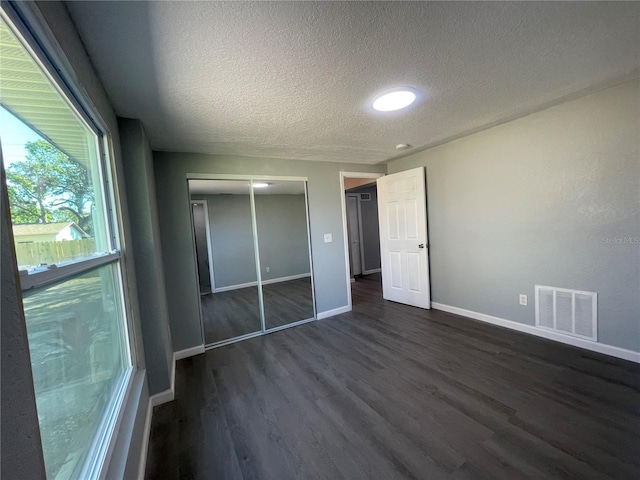 unfurnished bedroom featuring dark wood-style floors, a textured ceiling, visible vents, and baseboards