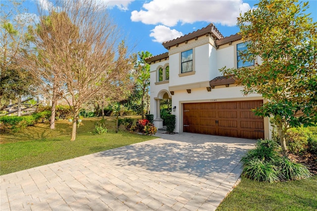 mediterranean / spanish-style house with stucco siding, a tile roof, an attached garage, decorative driveway, and a front yard