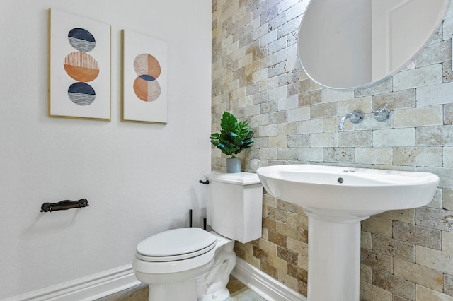 bathroom with brick wall, baseboards, and toilet