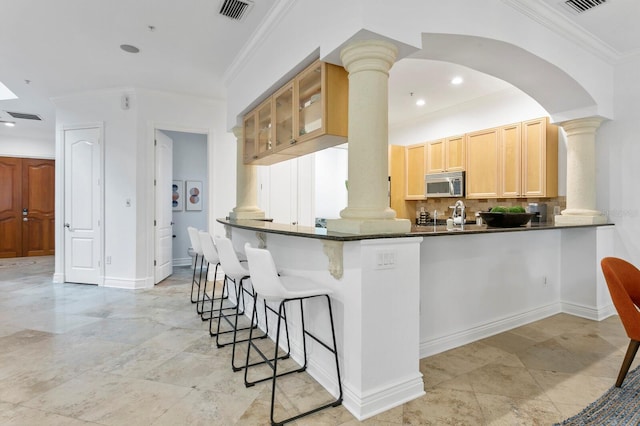 kitchen featuring stainless steel microwave, decorative columns, visible vents, and a kitchen breakfast bar