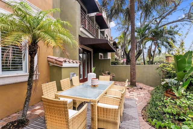 view of patio with outdoor dining area, fence, and a balcony