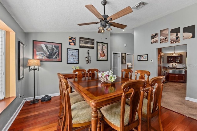 dining room featuring lofted ceiling, a textured ceiling, visible vents, and wood finished floors