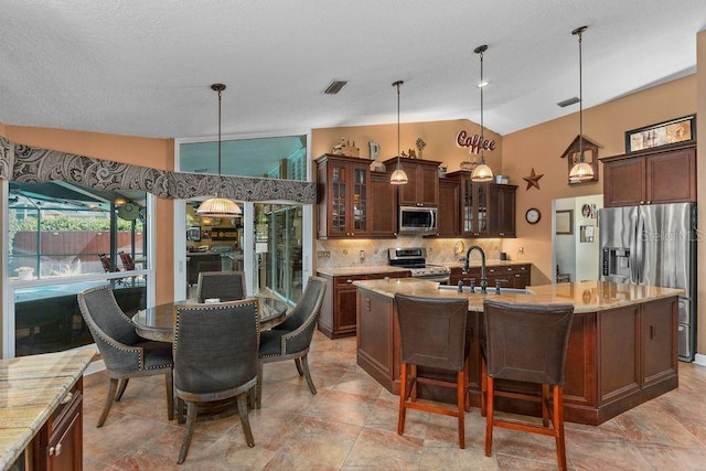 kitchen with a kitchen island with sink, stainless steel appliances, vaulted ceiling, backsplash, and glass insert cabinets