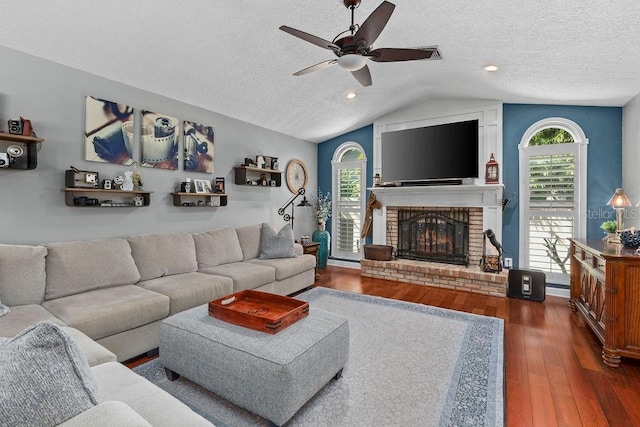 living area with a brick fireplace, a textured ceiling, vaulted ceiling, and wood finished floors