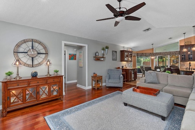 living room with lofted ceiling, ceiling fan, wood finished floors, visible vents, and baseboards