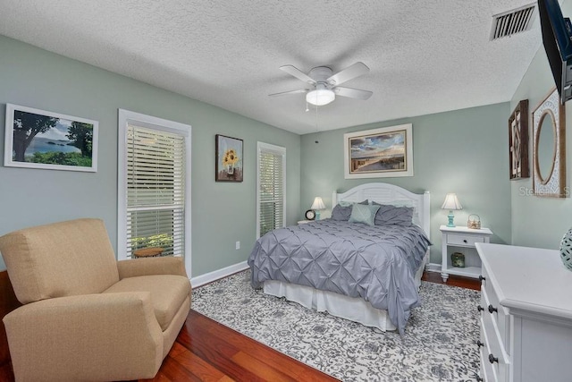 bedroom with visible vents, ceiling fan, a textured ceiling, wood finished floors, and baseboards