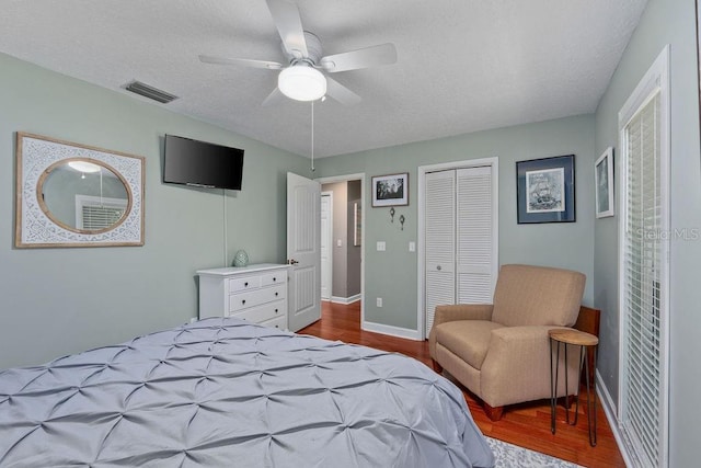 bedroom with a textured ceiling, wood finished floors, visible vents, baseboards, and a closet