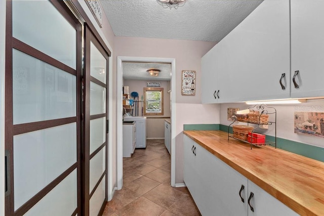 kitchen featuring a textured ceiling, light tile patterned floors, washing machine and dryer, butcher block counters, and white cabinets