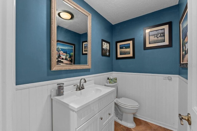 bathroom featuring a textured ceiling, toilet, a wainscoted wall, vanity, and tile patterned floors