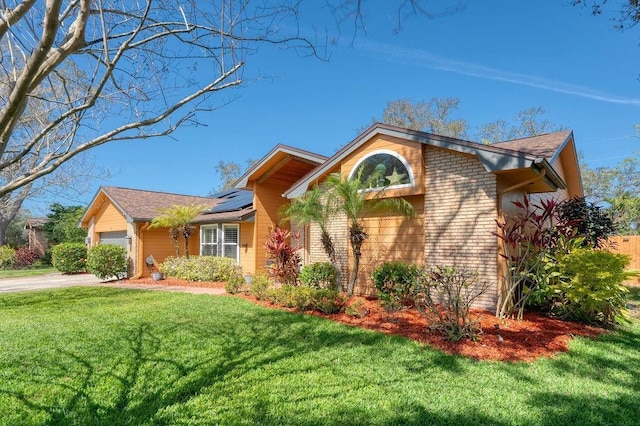 view of front of property with driveway, an attached garage, roof mounted solar panels, a front lawn, and brick siding