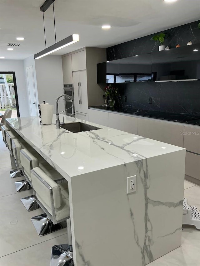 kitchen with a sink, visible vents, a large island, decorative backsplash, and modern cabinets