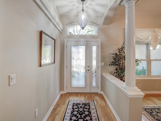 foyer entrance featuring baseboards, light wood-type flooring, and ornate columns