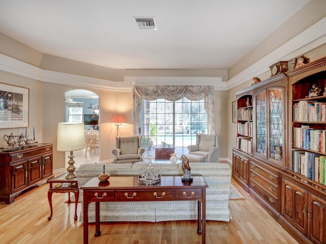 sitting room with arched walkways, light wood-style flooring, visible vents, and baseboards