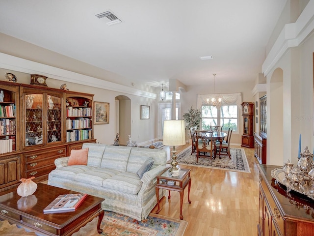 living room featuring light wood finished floors, visible vents, arched walkways, and a notable chandelier