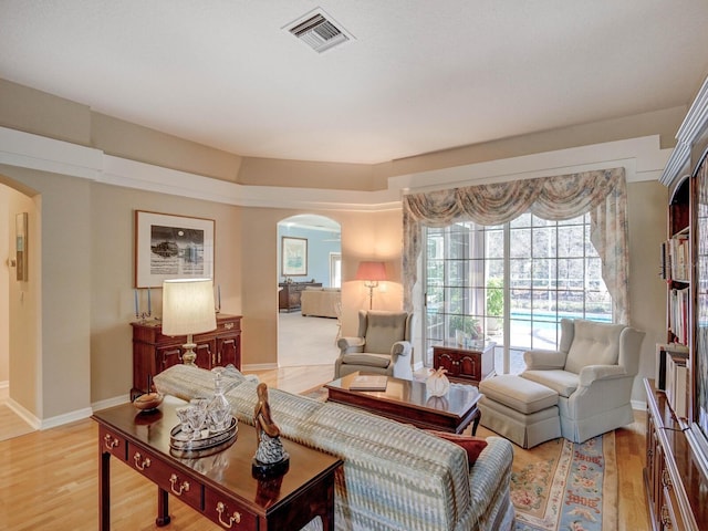 living area with arched walkways, light wood-type flooring, visible vents, and baseboards