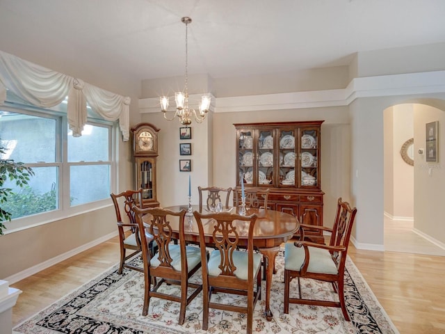 dining area with light wood-type flooring, arched walkways, a notable chandelier, and baseboards