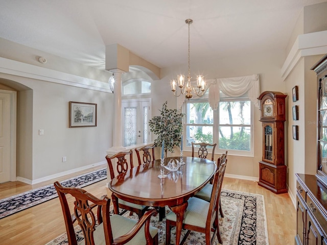 dining room with light wood-type flooring, a notable chandelier, arched walkways, and baseboards