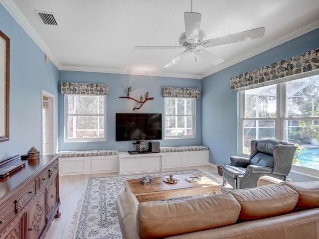 living area featuring ornamental molding, light wood-type flooring, visible vents, and a ceiling fan