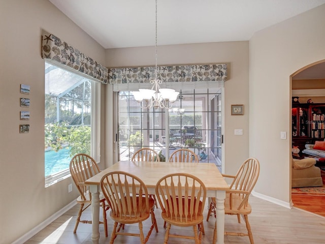 dining space with baseboards, plenty of natural light, light wood finished floors, and an inviting chandelier