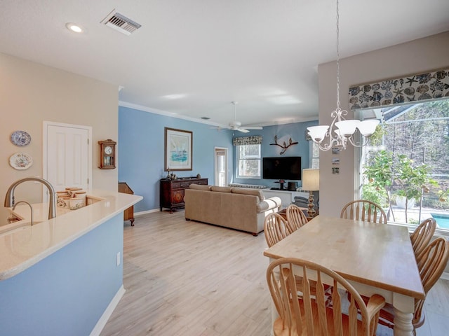 dining space with ceiling fan with notable chandelier, visible vents, baseboards, ornamental molding, and light wood finished floors