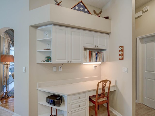 home office featuring light wood-style flooring, arched walkways, baseboards, and built in study area