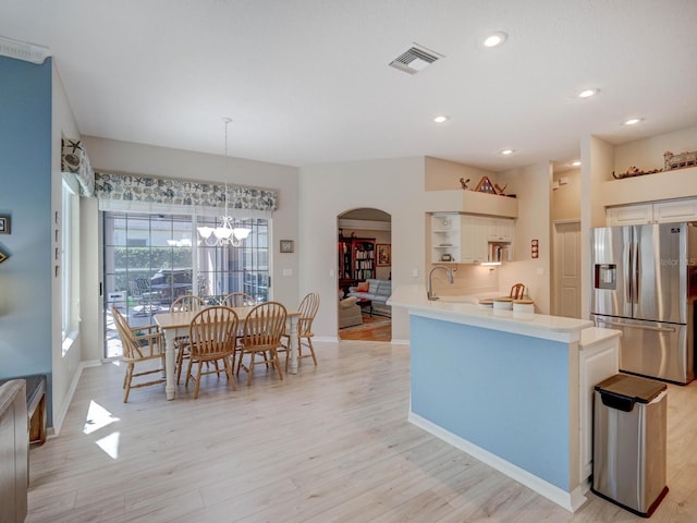 kitchen with arched walkways, light countertops, visible vents, light wood-style floors, and stainless steel fridge with ice dispenser