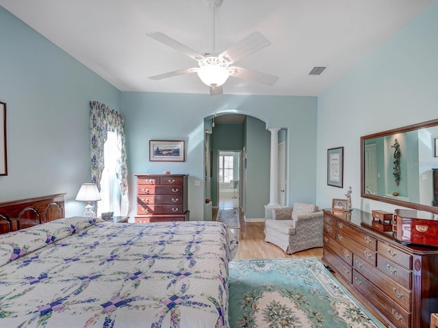 bedroom featuring arched walkways, ceiling fan, wood finished floors, visible vents, and decorative columns